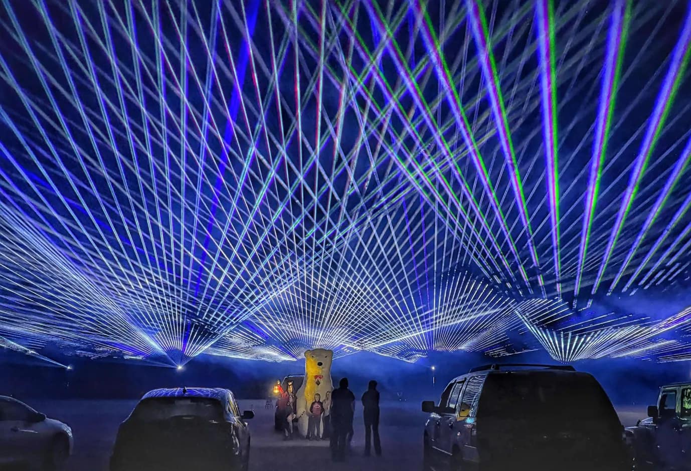 laser-3 People and cars under a night sky filled with crisscrossing blue and green laser lights.