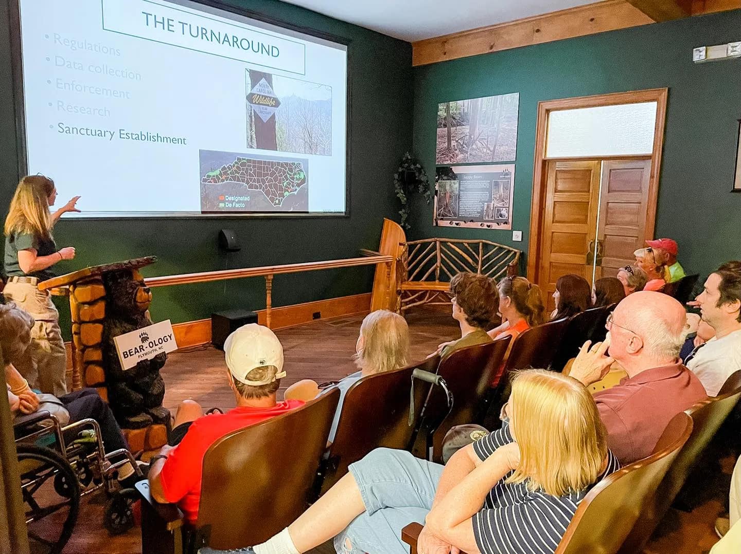 presentation-1 A woman presents a slideshow about bear conservation to an audience seated in a small lecture room.