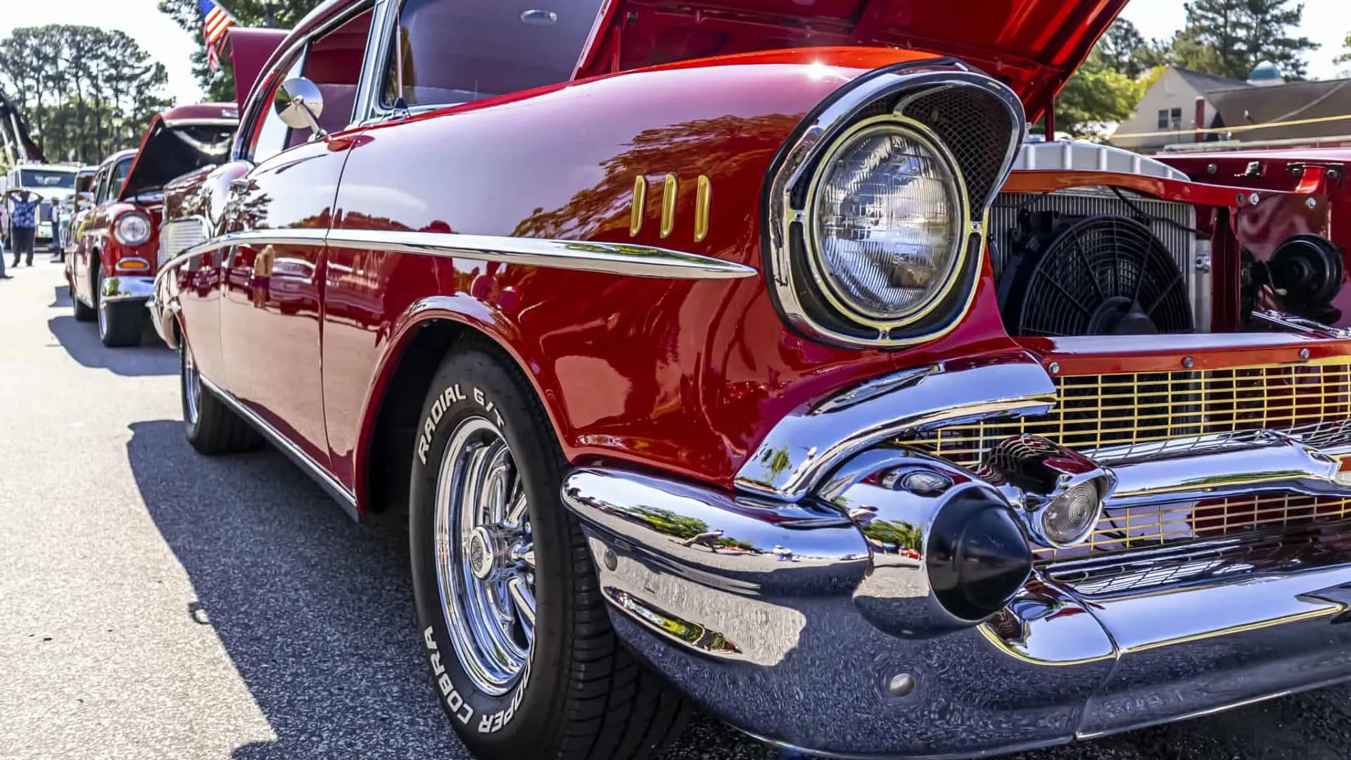 car-show-1 Close-up of a shiny red vintage car with hood open, showcasing chrome details at a car show.