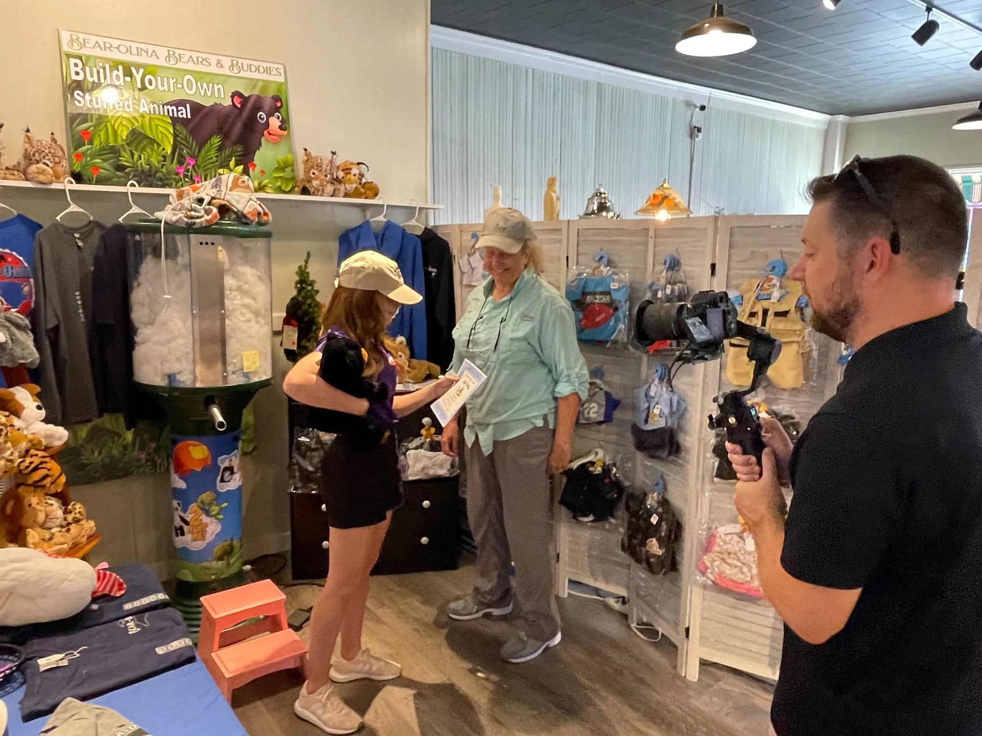 build-bear-2 Two women talk in a gift shop with plush toys as a man films them using a camera on a handheld stabilizer.